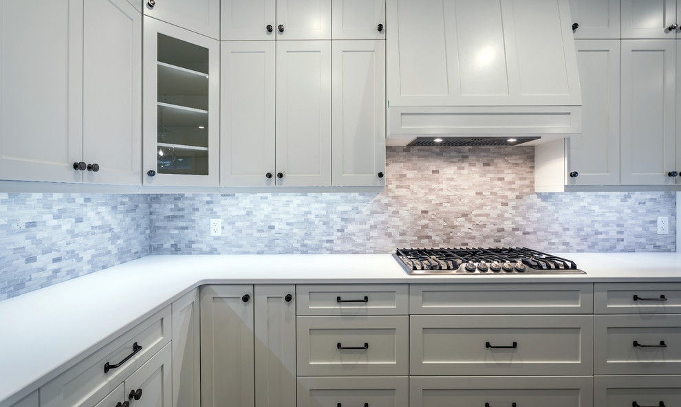 This is an example of a medium sized classic l-shaped open plan kitchen in Vancouver with a submerged sink, shaker cabinets, white cabinets, multi-coloured splashback, glass tiled splashback, stainless steel appliances, laminate floors, an island, brown floors, white worktops and quartz worktops.