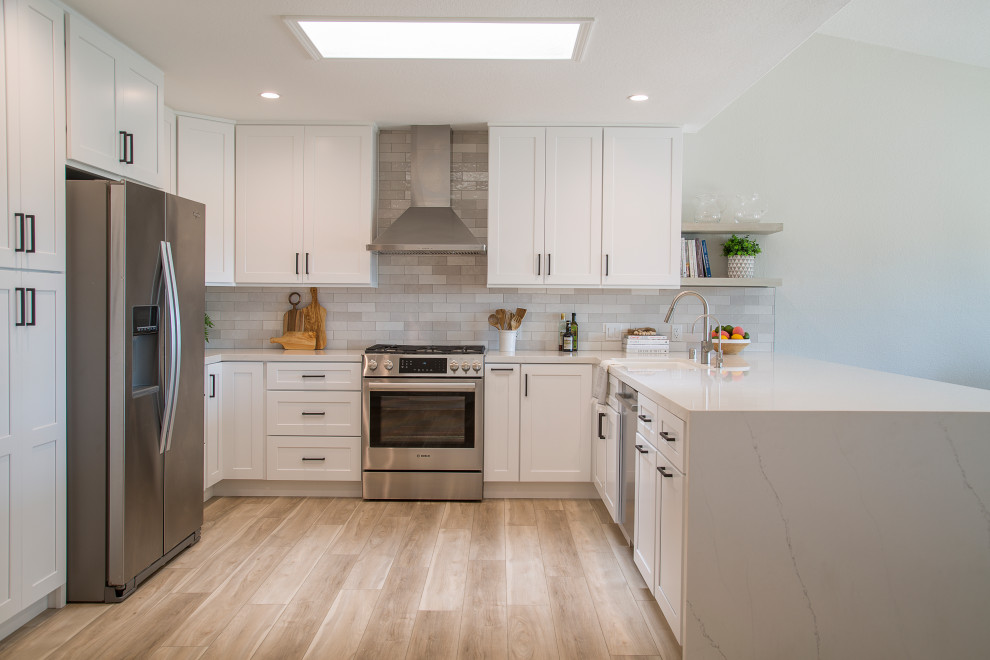 Photo of a medium sized traditional l-shaped open plan kitchen in Orange County with a submerged sink, shaker cabinets, white cabinets, engineered stone countertops, grey splashback, metro tiled splashback, stainless steel appliances, laminate floors, no island, brown floors, white worktops and a vaulted ceiling.