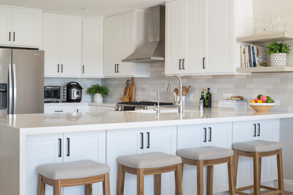 Idée de décoration pour une cuisine ouverte tradition en L de taille moyenne avec un évier encastré, un placard à porte shaker, des portes de placard blanches, un plan de travail en quartz modifié, une crédence grise, une crédence en carrelage métro, un électroménager en acier inoxydable, sol en stratifié, aucun îlot, un sol marron, un plan de travail blanc et un plafond voûté.