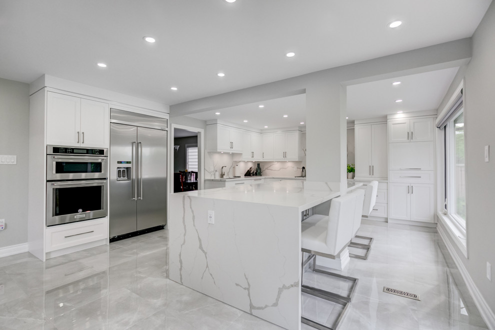 This is an example of a large contemporary l-shaped kitchen/diner in Toronto with a submerged sink, shaker cabinets, white cabinets, marble worktops, white splashback, stone slab splashback, stainless steel appliances, marble flooring, an island, grey floors and white worktops.
