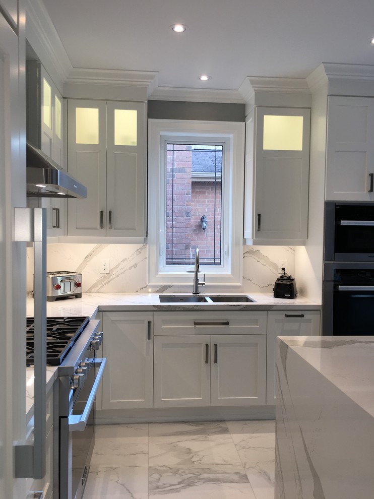 Example of a large transitional l-shaped porcelain tile and white floor enclosed kitchen design in Toronto with an undermount sink, shaker cabinets, white cabinets, quartz countertops, white backsplash, stone slab backsplash, stainless steel appliances, an island and white countertops