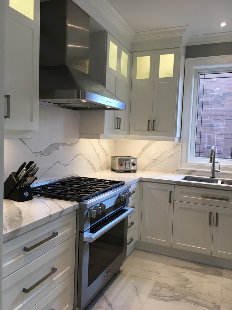 This is an example of a large traditional l-shaped enclosed kitchen in Toronto with a submerged sink, shaker cabinets, white cabinets, engineered stone countertops, white splashback, stone slab splashback, stainless steel appliances, porcelain flooring, an island, white floors and white worktops.