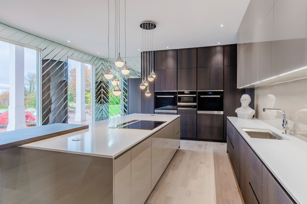 Large contemporary u-shaped enclosed kitchen in Other with dark wood cabinets, engineered stone countertops, glass sheet splashback, light hardwood flooring, an island, white worktops, a submerged sink, flat-panel cabinets, beige splashback, black appliances and beige floors.
