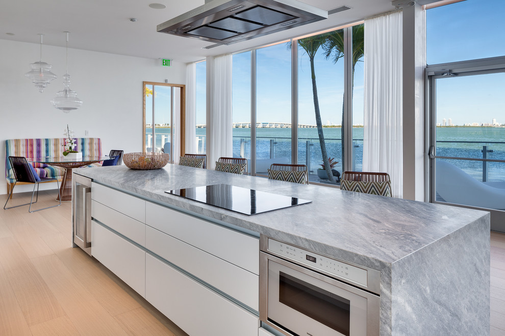 Open concept kitchen - large modern single-wall porcelain tile and beige floor open concept kitchen idea in Miami with an undermount sink, flat-panel cabinets, white cabinets, mirror backsplash, stainless steel appliances, an island and gray countertops