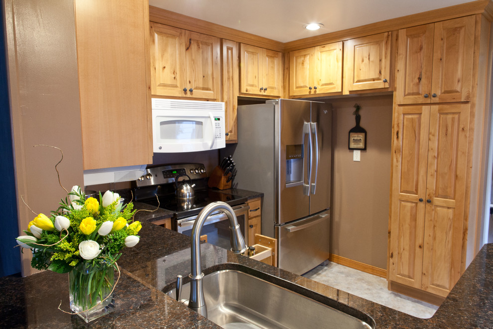 Exemple d'une petite cuisine chic en U et bois clair avec un évier encastré, un placard avec porte à panneau surélevé, un plan de travail en granite et un électroménager en acier inoxydable.