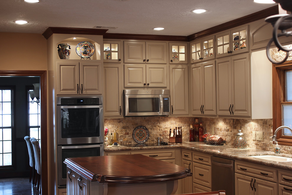 Large elegant l-shaped terra-cotta tile eat-in kitchen photo in Houston with an undermount sink, raised-panel cabinets, white cabinets, granite countertops, beige backsplash, stone tile backsplash, stainless steel appliances and an island