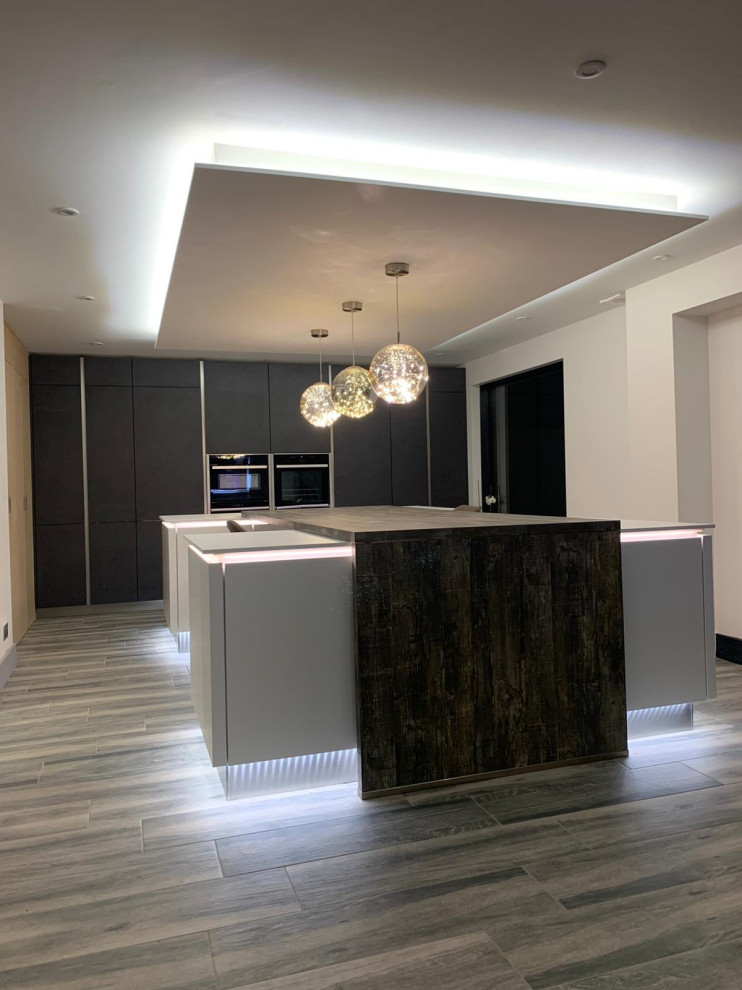Photo of a large modern u-shaped kitchen/diner in London with flat-panel cabinets, grey cabinets, composite countertops, dark hardwood flooring, an island, brown floors and grey worktops.