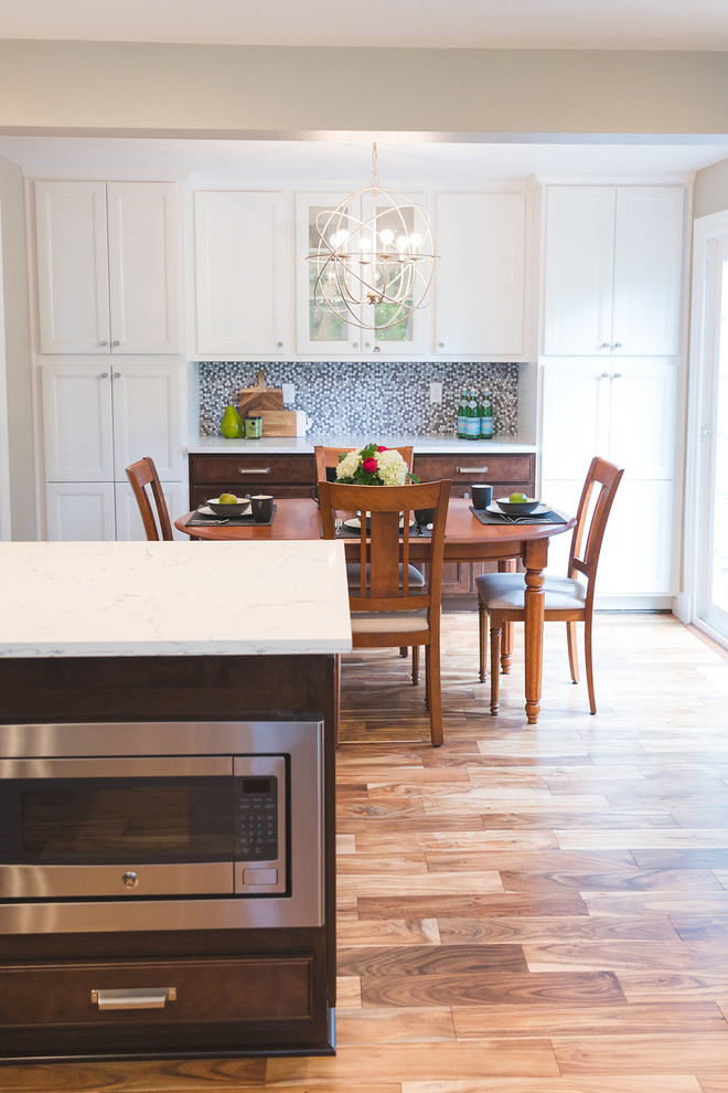 Example of a mid-sized transitional u-shaped medium tone wood floor and brown floor eat-in kitchen design in Seattle with a farmhouse sink, recessed-panel cabinets, white cabinets, quartzite countertops, gray backsplash, mosaic tile backsplash, stainless steel appliances and a peninsula