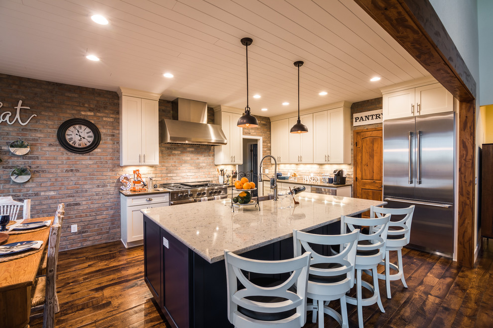Foto på ett mellanstort lantligt grå kök, med en rustik diskho, skåp i shakerstil, vita skåp, bänkskiva i kvarts, grått stänkskydd, stänkskydd i tegel, rostfria vitvaror, mellanmörkt trägolv, en köksö och brunt golv