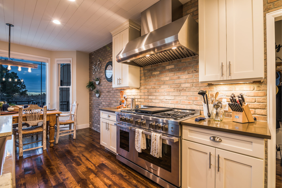 Inspiration for a mid-sized cottage galley medium tone wood floor and brown floor eat-in kitchen remodel in Denver with a farmhouse sink, shaker cabinets, white cabinets, quartz countertops, gray backsplash, brick backsplash, stainless steel appliances, an island and gray countertops