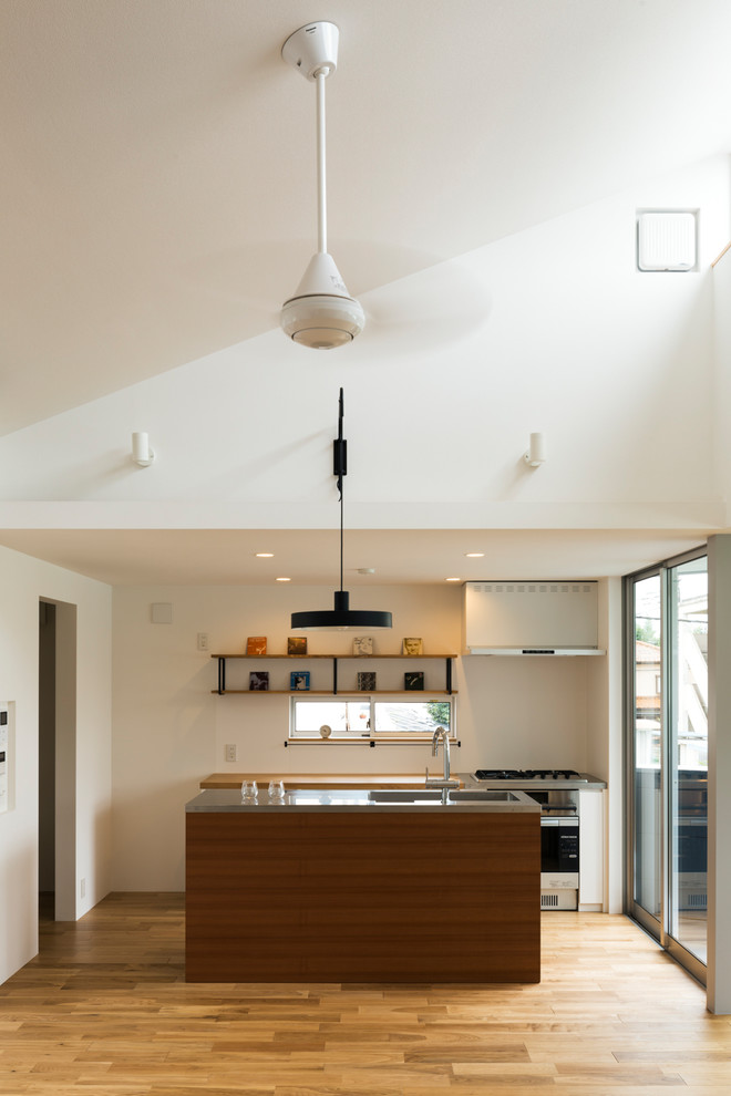 Idee per una cucina moderna con lavello a vasca singola, top in acciaio inossidabile, paraspruzzi bianco, pavimento in legno massello medio e pavimento marrone