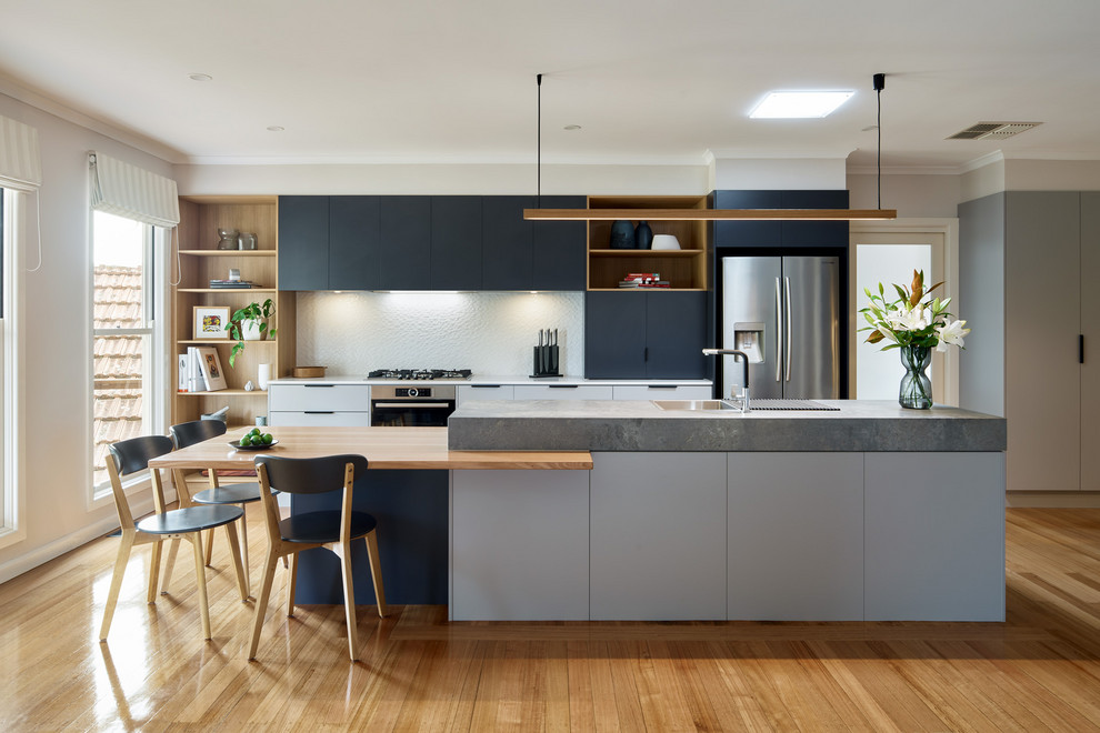 Design ideas for a contemporary kitchen in Melbourne with flat-panel cabinets, white splashback, stainless steel appliances, light hardwood flooring, an island, beige floors and white worktops.
