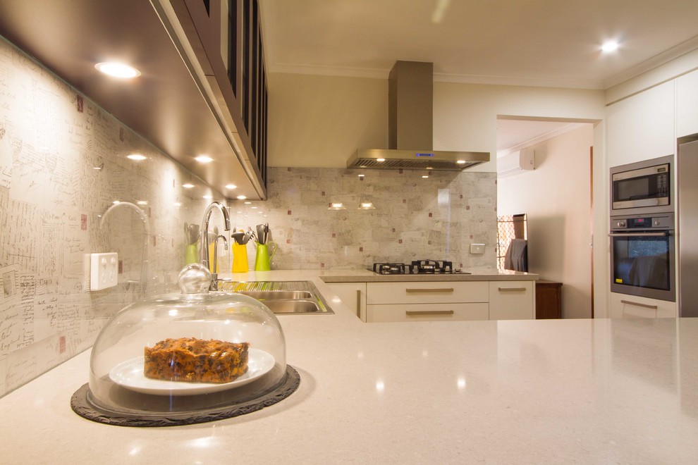 Foto di una cucina design di medie dimensioni con ante lisce, ante bianche, top in quarzo composito, elettrodomestici in acciaio inossidabile e penisola