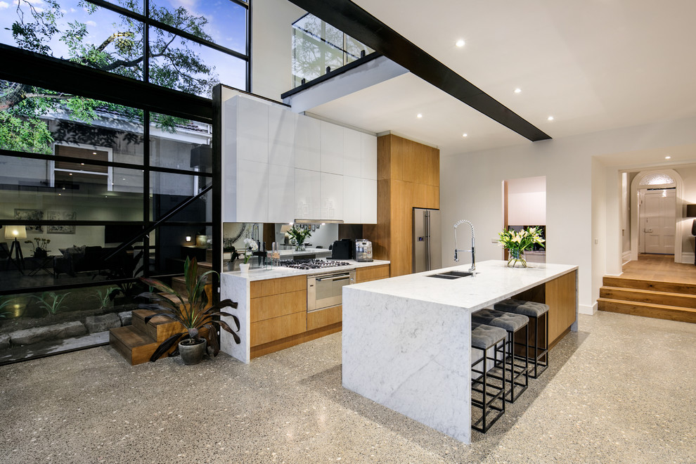 Example of a mid-sized galley concrete floor eat-in kitchen design in Melbourne with an integrated sink, white cabinets, glass sheet backsplash, stainless steel appliances and an island