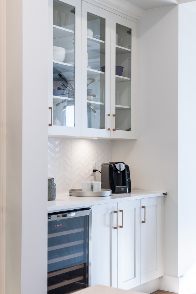 Design ideas for a large classic single-wall kitchen pantry in Vancouver with recessed-panel cabinets, white cabinets, engineered stone countertops, white splashback, porcelain splashback, stainless steel appliances, medium hardwood flooring, brown floors and white worktops.