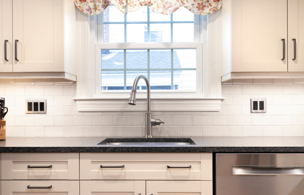 Foto på ett mellanstort vintage svart kök, med en enkel diskho, släta luckor, vita skåp, granitbänkskiva, vitt stänkskydd, stänkskydd i keramik, rostfria vitvaror, mellanmörkt trägolv, en köksö och gult golv