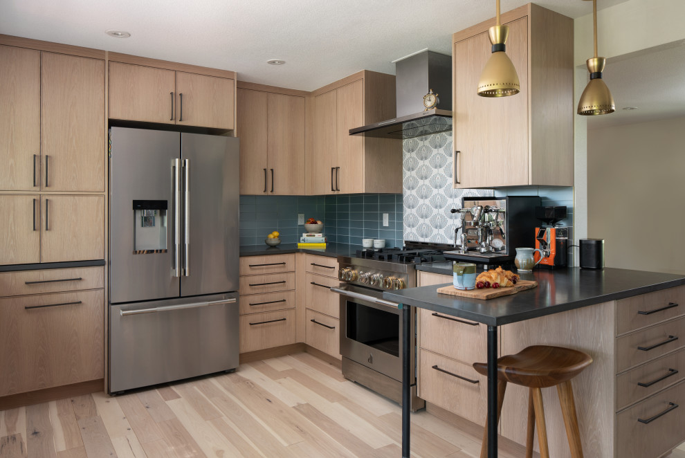 Geschlossene Eklektische Küche in U-Form mit hellen Holzschränken, Quarzwerkstein-Arbeitsplatte, Küchenrückwand in Blau, Rückwand aus Glasfliesen, Küchengeräten aus Edelstahl, hellem Holzboden und schwarzer Arbeitsplatte in Denver
