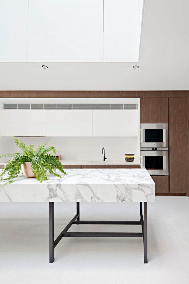 На фото: параллельная кухня в современном стиле с плоскими фасадами, темными деревянными фасадами, техникой из нержавеющей стали, островом, серым полом и белой столешницей