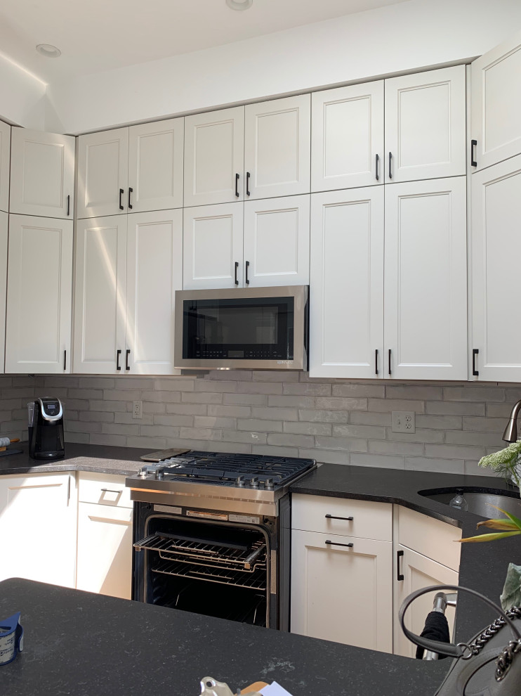 Example of a small transitional l-shaped medium tone wood floor enclosed kitchen design in Boston with an undermount sink, shaker cabinets, white cabinets, quartz countertops, white backsplash, subway tile backsplash, stainless steel appliances, a peninsula and black countertops