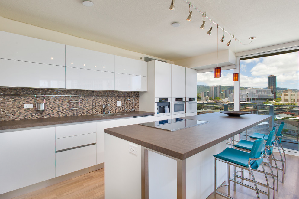 Zweizeilige Moderne Küche mit Einbauwaschbecken, flächenbündigen Schrankfronten, weißen Schränken, Küchenrückwand in Braun, Rückwand aus Mosaikfliesen, weißen Elektrogeräten, braunem Holzboden und Kücheninsel in Hawaii