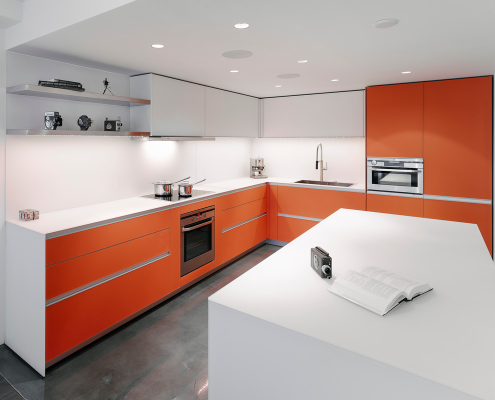 Пример оригинального дизайна: угловая кухня-гостиная среднего размера в современном стиле с врезной мойкой, плоскими фасадами, оранжевыми фасадами, белым фартуком, техникой из нержавеющей стали, бетонным полом и островом