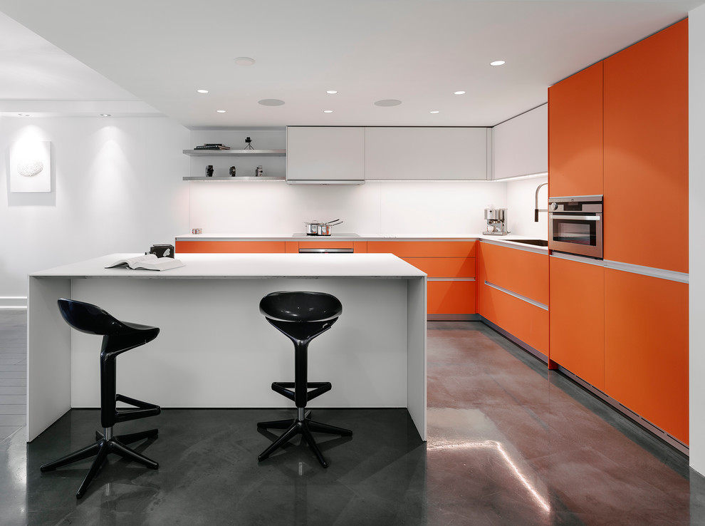 Свежая идея для дизайна: угловая кухня-гостиная среднего размера в современном стиле с врезной мойкой, плоскими фасадами, оранжевыми фасадами, белым фартуком, техникой из нержавеющей стали, бетонным полом и островом - отличное фото интерьера