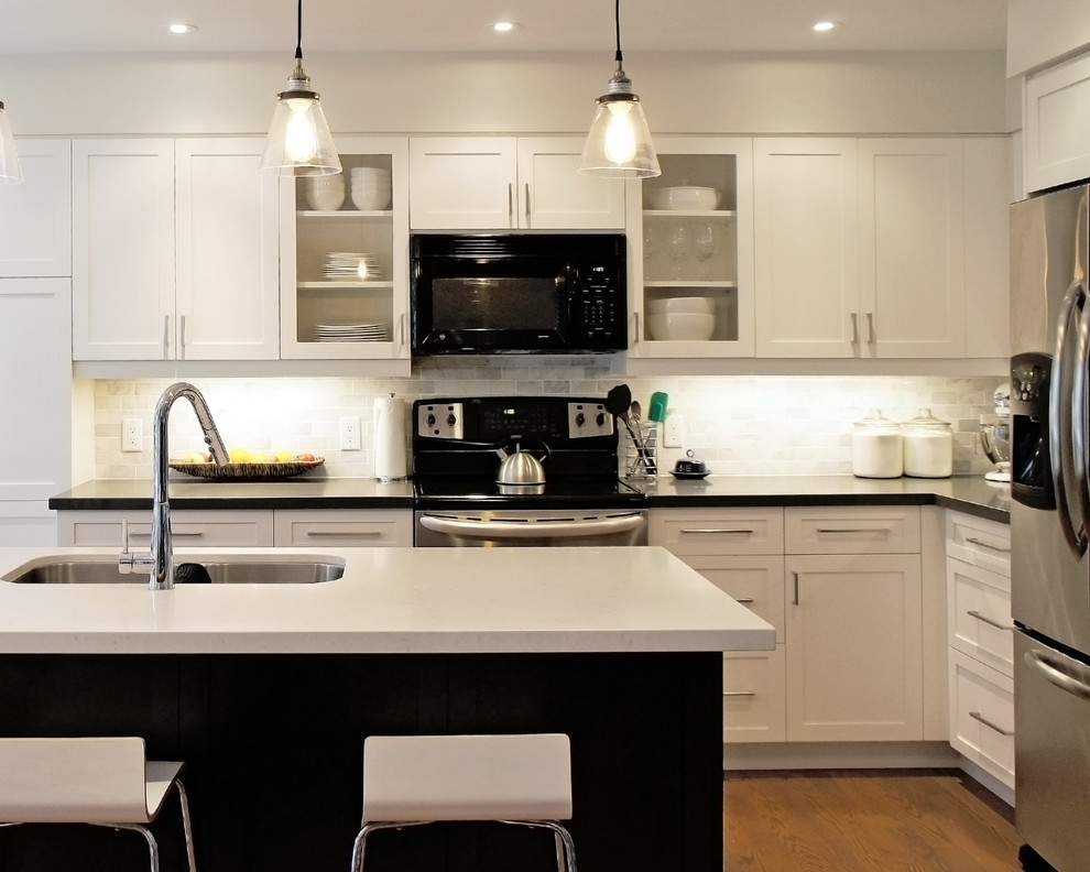 Mid-sized transitional l-shaped medium tone wood floor open concept kitchen photo in Toronto with an undermount sink, recessed-panel cabinets, white cabinets, quartz countertops, beige backsplash, stone tile backsplash, an island and stainless steel appliances