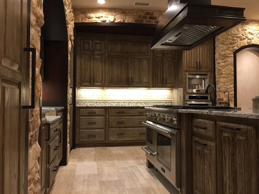 Bild på ett mellanstort medelhavsstil kök och matrum, med en rustik diskho, luckor med upphöjd panel, skåp i slitet trä, granitbänkskiva, beige stänkskydd, stänkskydd i stenkakel, rostfria vitvaror, travertin golv och en köksö