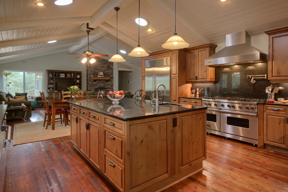 Example of a large country u-shaped medium tone wood floor and brown floor open concept kitchen design in Other with a farmhouse sink, raised-panel cabinets, medium tone wood cabinets, granite countertops, black backsplash, stone slab backsplash, stainless steel appliances and an island
