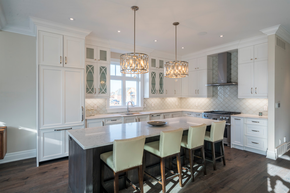 Photo of a large classic l-shaped kitchen in Toronto with a submerged sink, recessed-panel cabinets, white cabinets, quartz worktops, white splashback, ceramic splashback, integrated appliances, medium hardwood flooring, an island and brown floors.