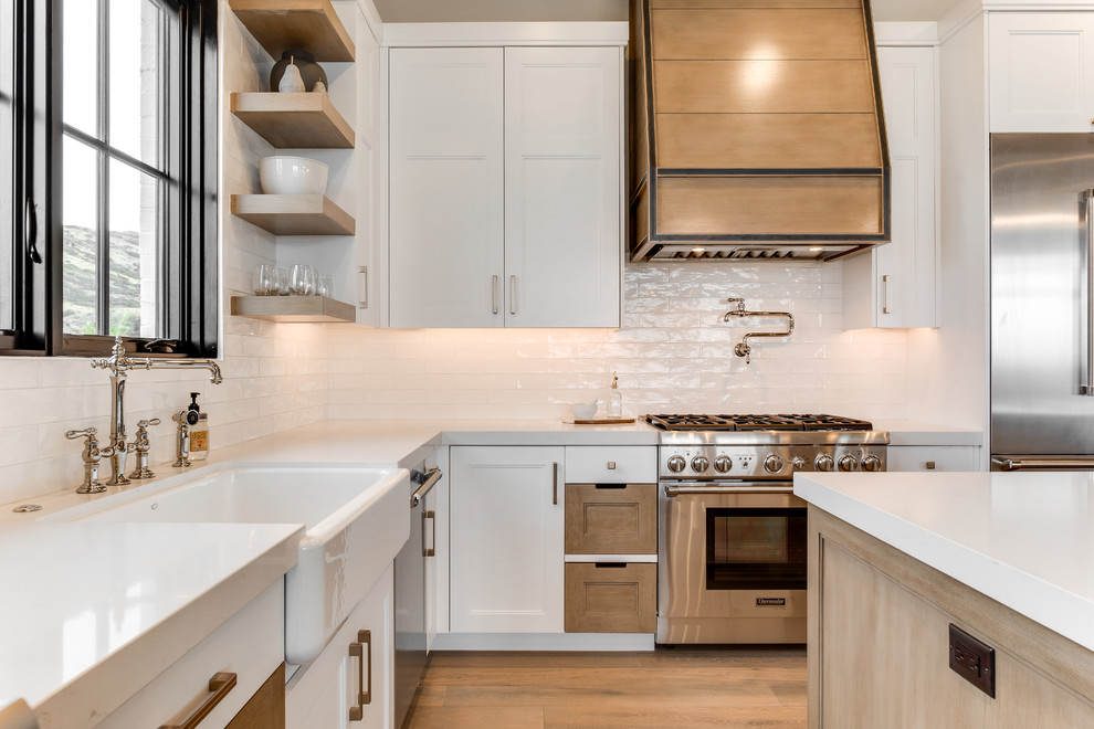 Example of a cottage light wood floor eat-in kitchen design in Salt Lake City with flat-panel cabinets, white backsplash, stainless steel appliances, an island and white countertops