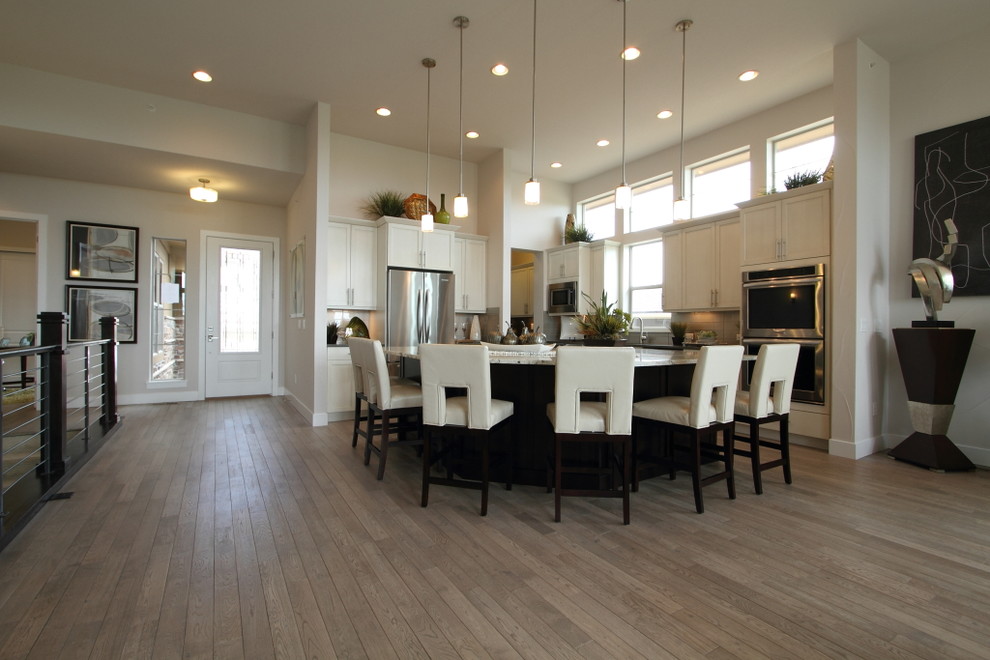 Open concept kitchen - mid-sized transitional l-shaped light wood floor and brown floor open concept kitchen idea in Denver with an undermount sink, shaker cabinets, white cabinets, beige backsplash, glass tile backsplash, stainless steel appliances, quartz countertops and an island