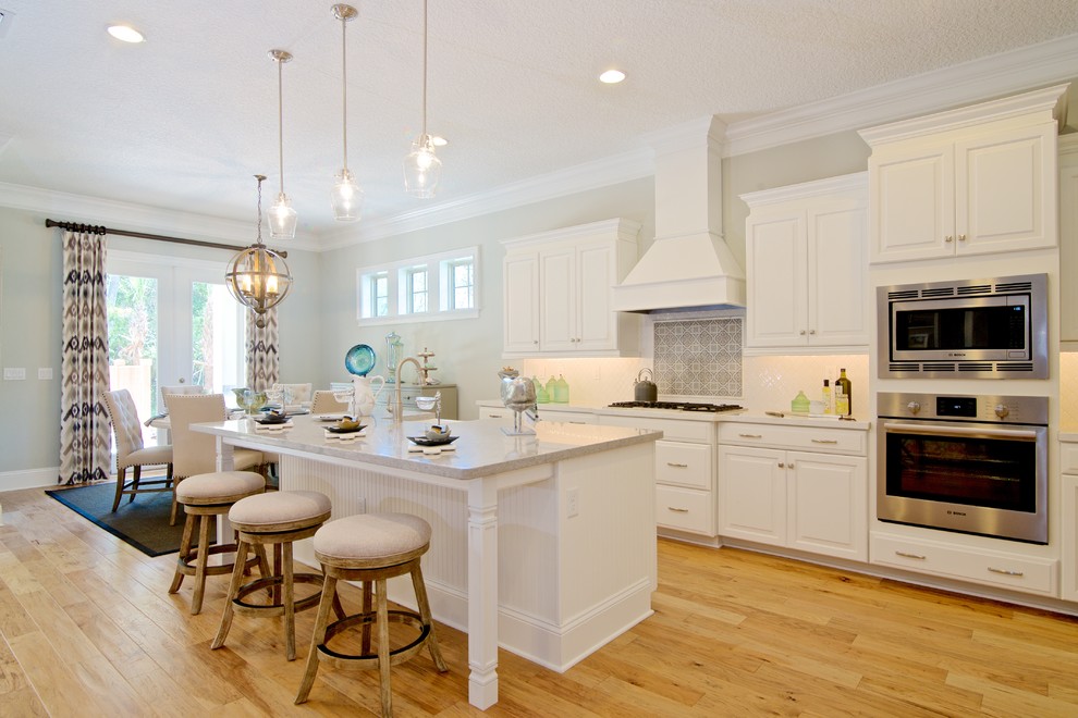 Kitchen pantry - mid-sized mediterranean l-shaped light wood floor kitchen pantry idea in Jacksonville with an undermount sink, raised-panel cabinets, white cabinets, quartz countertops, white backsplash, ceramic backsplash, stainless steel appliances and an island
