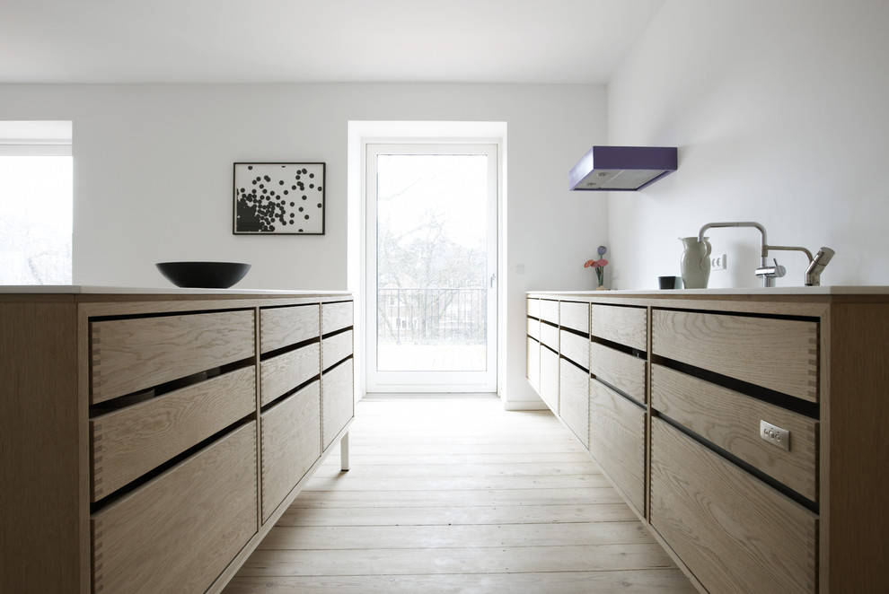 Inspiration pour une cuisine américaine parallèle minimaliste en bois clair avec un évier encastré, un plan de travail en surface solide, une crédence blanche et un électroménager en acier inoxydable.