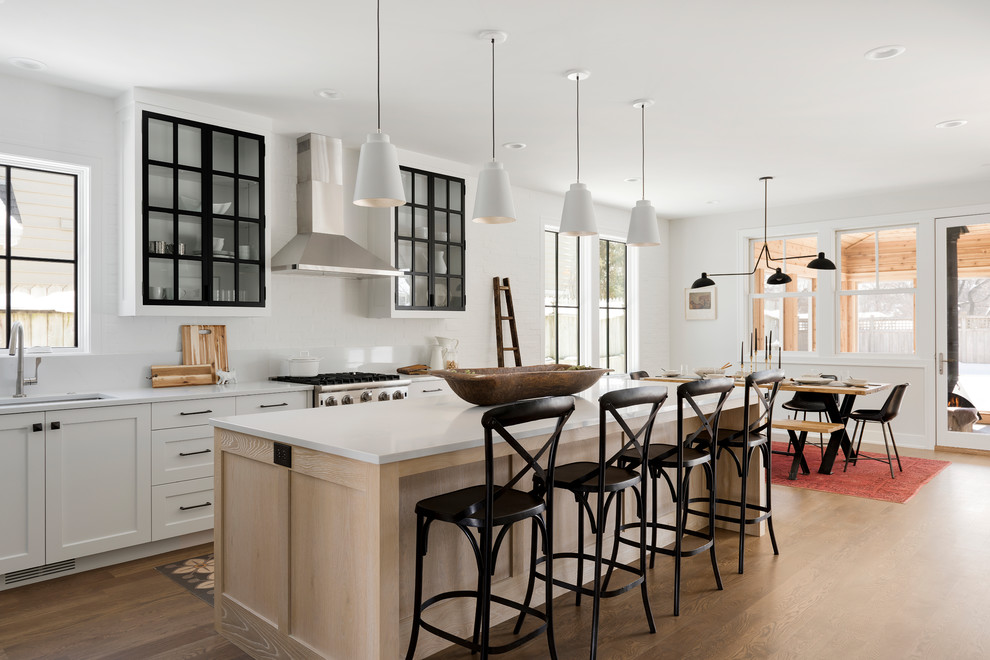 Landhausstil Wohnküche mit Schrankfronten im Shaker-Stil, Küchenrückwand in Weiß, Küchengeräten aus Edelstahl, braunem Holzboden, Kücheninsel und weißer Arbeitsplatte in Minneapolis