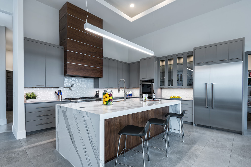 Contemporary l-shaped kitchen in Austin with a submerged sink, flat-panel cabinets, grey cabinets, white splashback, stainless steel appliances, an island and grey floors.