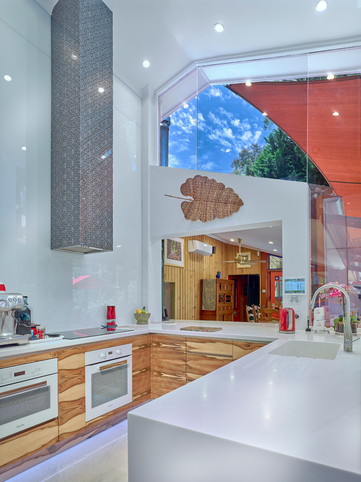 他の地域にあるラグジュアリーな中くらいなコンテンポラリースタイルのおしゃれなコの字型キッチン (中間色木目調キャビネット、白いキッチンパネル、ガラス板のキッチンパネル、白い調理設備) の写真
