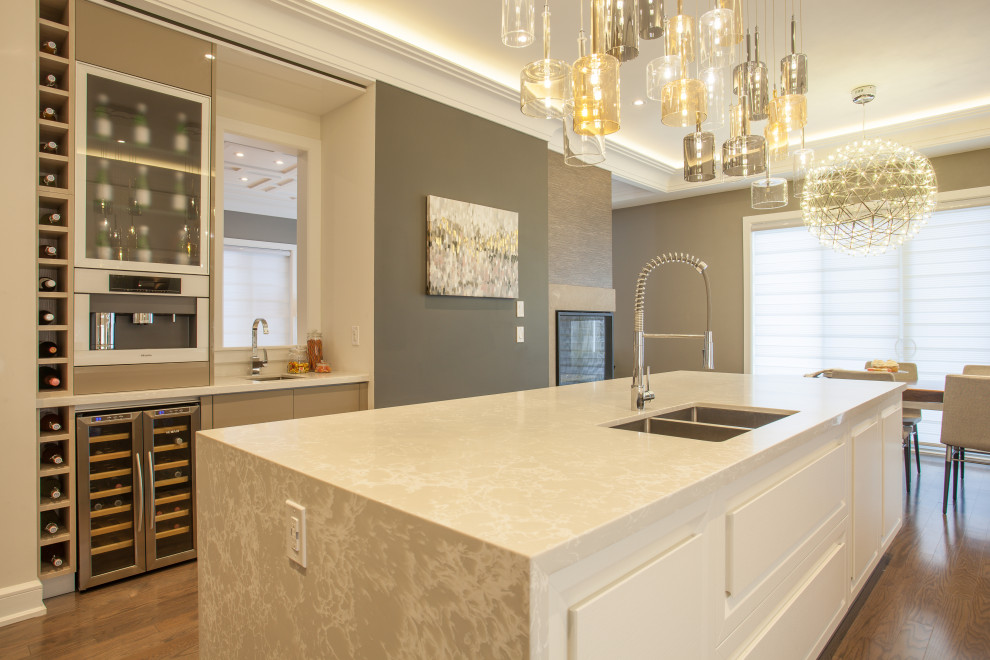 This is an example of a large modern l-shaped kitchen/diner in Toronto with a submerged sink, shaker cabinets, white cabinets, quartz worktops, beige splashback, stone tiled splashback, white appliances, medium hardwood flooring, an island, brown floors, beige worktops and a drop ceiling.