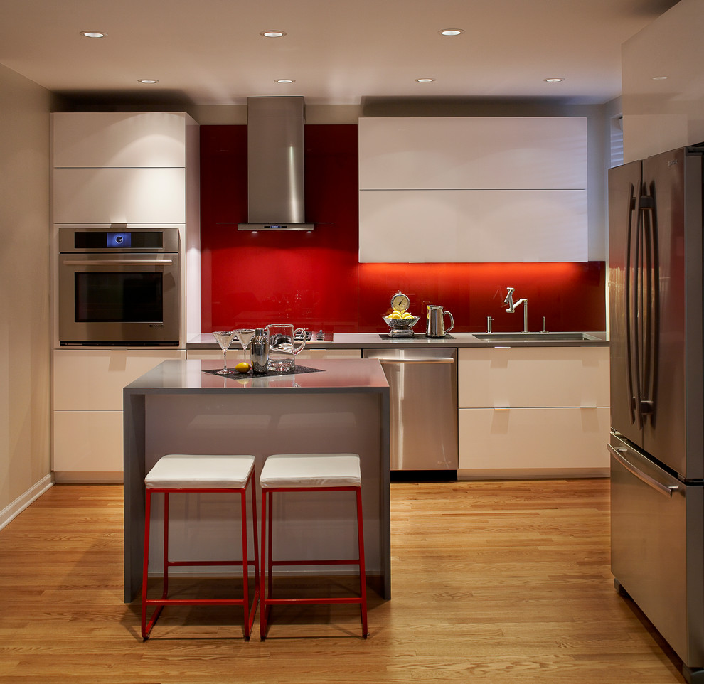 Modelo de cocina minimalista con armarios con paneles lisos, puertas de armario blancas, salpicadero rojo y electrodomésticos de acero inoxidable