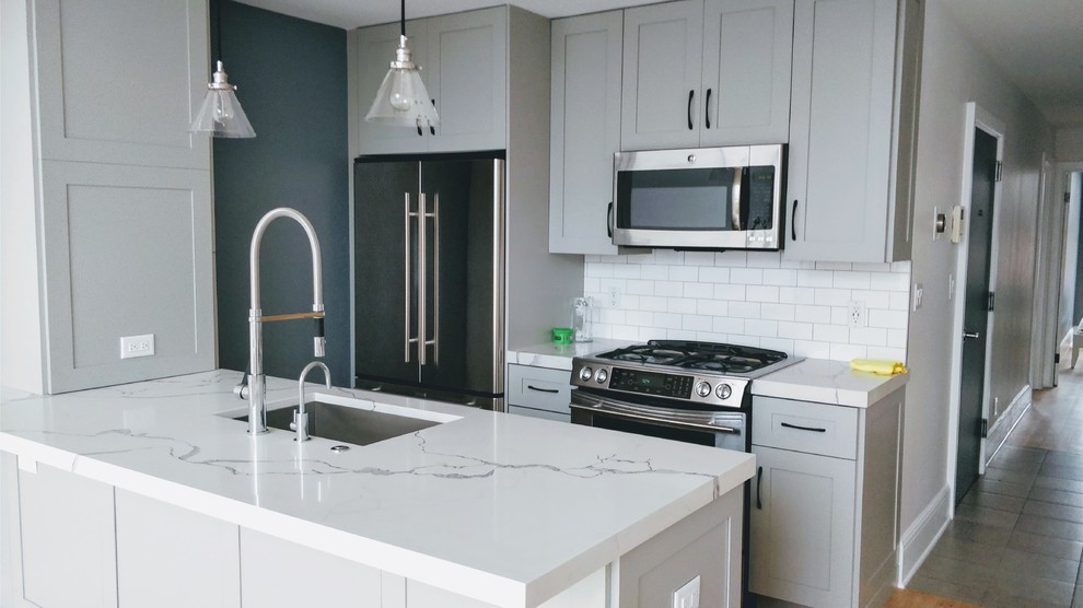 Small minimalist galley light wood floor and brown floor eat-in kitchen photo in New York with an undermount sink, shaker cabinets, gray cabinets, quartz countertops, stainless steel appliances, white backsplash, subway tile backsplash, an island and white countertops