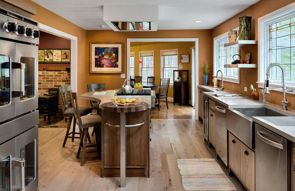 Kitchen - mid-sized craftsman galley light wood floor kitchen idea in Portland Maine with a farmhouse sink, flat-panel cabinets, medium tone wood cabinets, stainless steel countertops, orange backsplash, stainless steel appliances and an island