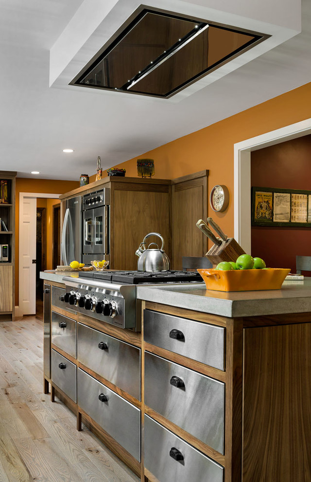 This is an example of a medium sized classic l-shaped kitchen in Portland Maine with flat-panel cabinets, stainless steel cabinets, concrete worktops, stainless steel appliances, light hardwood flooring and an island.