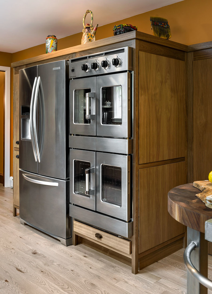 Imagen de cocina de estilo americano de tamaño medio con fregadero sobremueble, armarios con paneles lisos, puertas de armario de madera oscura, encimera de acero inoxidable, salpicadero naranja, electrodomésticos de acero inoxidable, suelo de madera clara y una isla