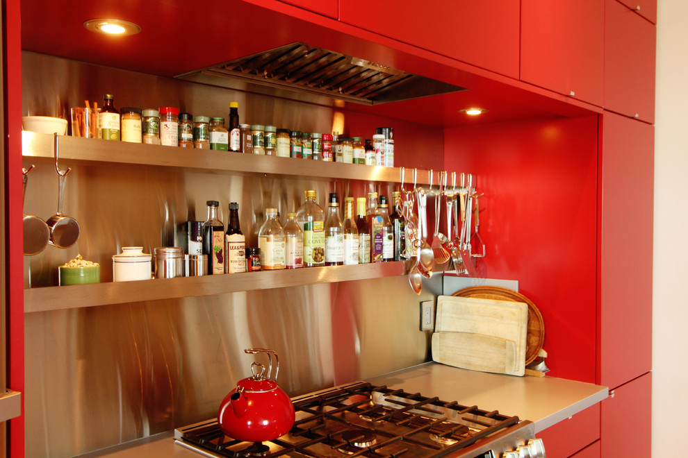 Immagine di una piccola cucina moderna con lavello sottopiano, ante lisce, ante rosse, top in superficie solida, paraspruzzi con piastrelle di metallo, elettrodomestici in acciaio inossidabile e pavimento in legno massello medio