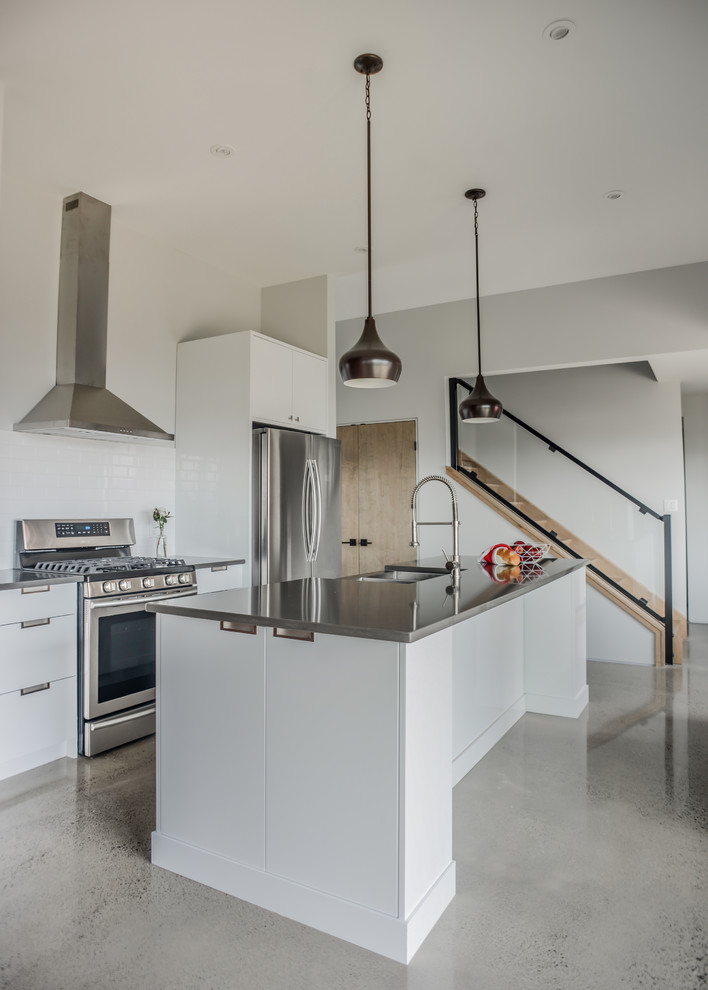 Example of a trendy galley concrete floor and gray floor enclosed kitchen design in Toronto with a farmhouse sink, flat-panel cabinets, white cabinets, solid surface countertops, white backsplash, stone tile backsplash, stainless steel appliances and an island