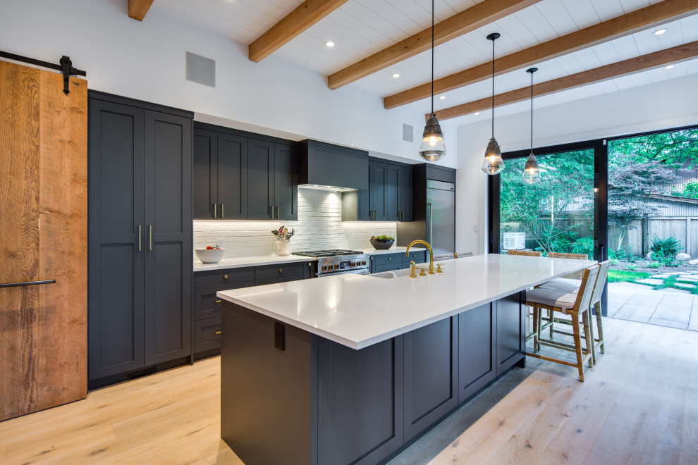 Example of a mid-sized minimalist galley light wood floor and beige floor eat-in kitchen design in Vancouver with a farmhouse sink, shaker cabinets, black cabinets, quartz countertops, white backsplash, subway tile backsplash, stainless steel appliances, an island and white countertops