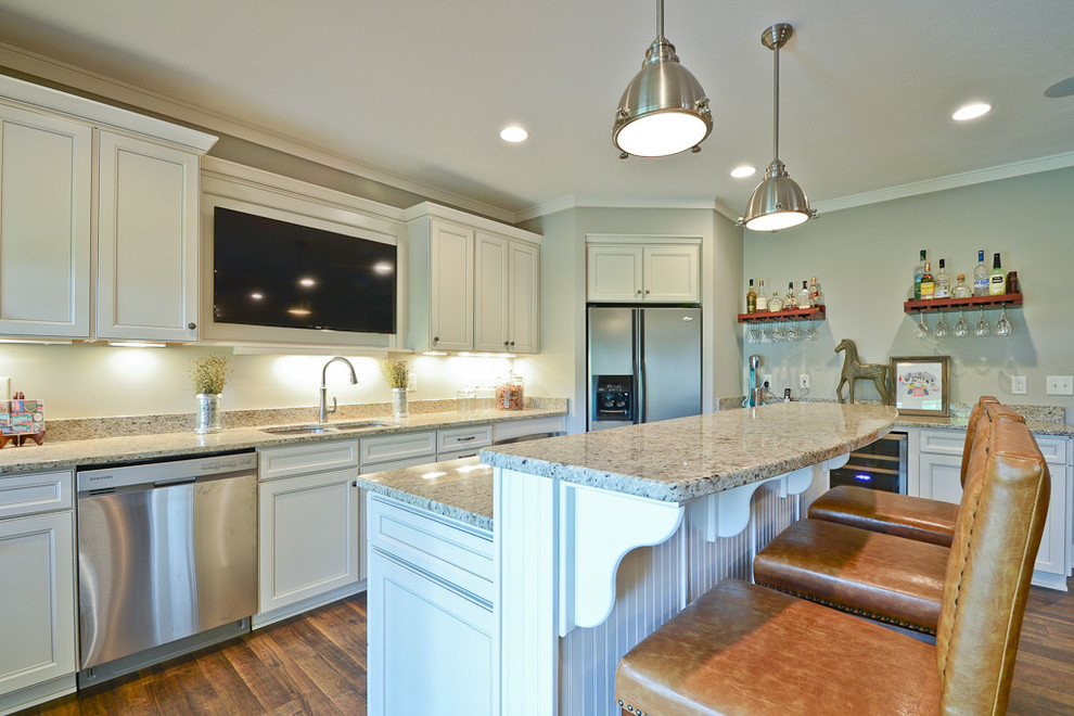 Modern inredning av ett stort kök, med en undermonterad diskho, luckor med infälld panel, vita skåp, granitbänkskiva, rostfria vitvaror, mellanmörkt trägolv och en köksö