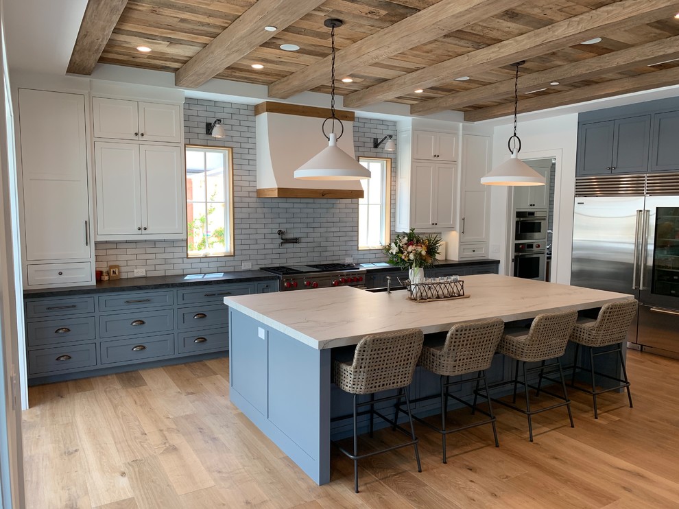Inspiration for a nautical l-shaped kitchen/diner in Orange County with shaker cabinets, white cabinets, white splashback, metro tiled splashback, stainless steel appliances, medium hardwood flooring, an island, brown floors and white worktops.