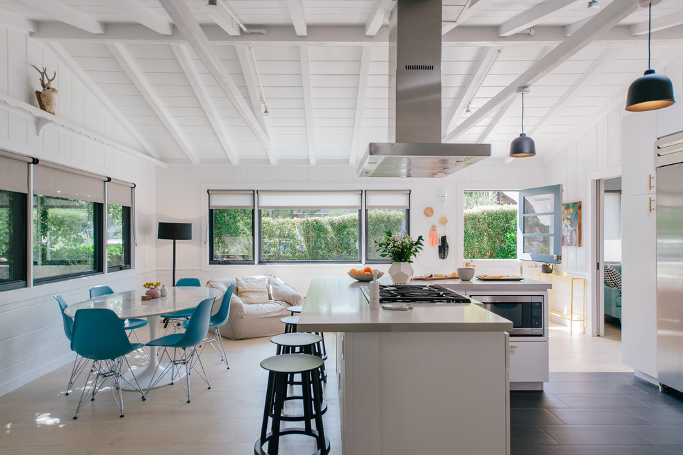 Photo of a small l-shaped open plan kitchen in Orange County with flat-panel cabinets, white cabinets, engineered stone countertops, stainless steel appliances, an island, grey worktops, black floors, exposed beams, a submerged sink and porcelain flooring.