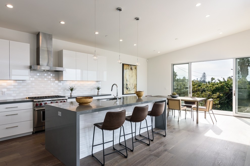Moderne Küche mit Unterbauwaschbecken, flächenbündigen Schrankfronten, weißen Schränken, Küchenrückwand in Weiß, Rückwand aus Metrofliesen, Küchengeräten aus Edelstahl, dunklem Holzboden und Kücheninsel in San Diego